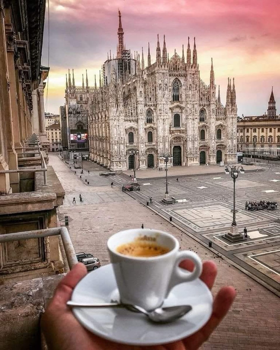 Espresso in a white cup held above Piazza del Duomo in Milan at sunrise