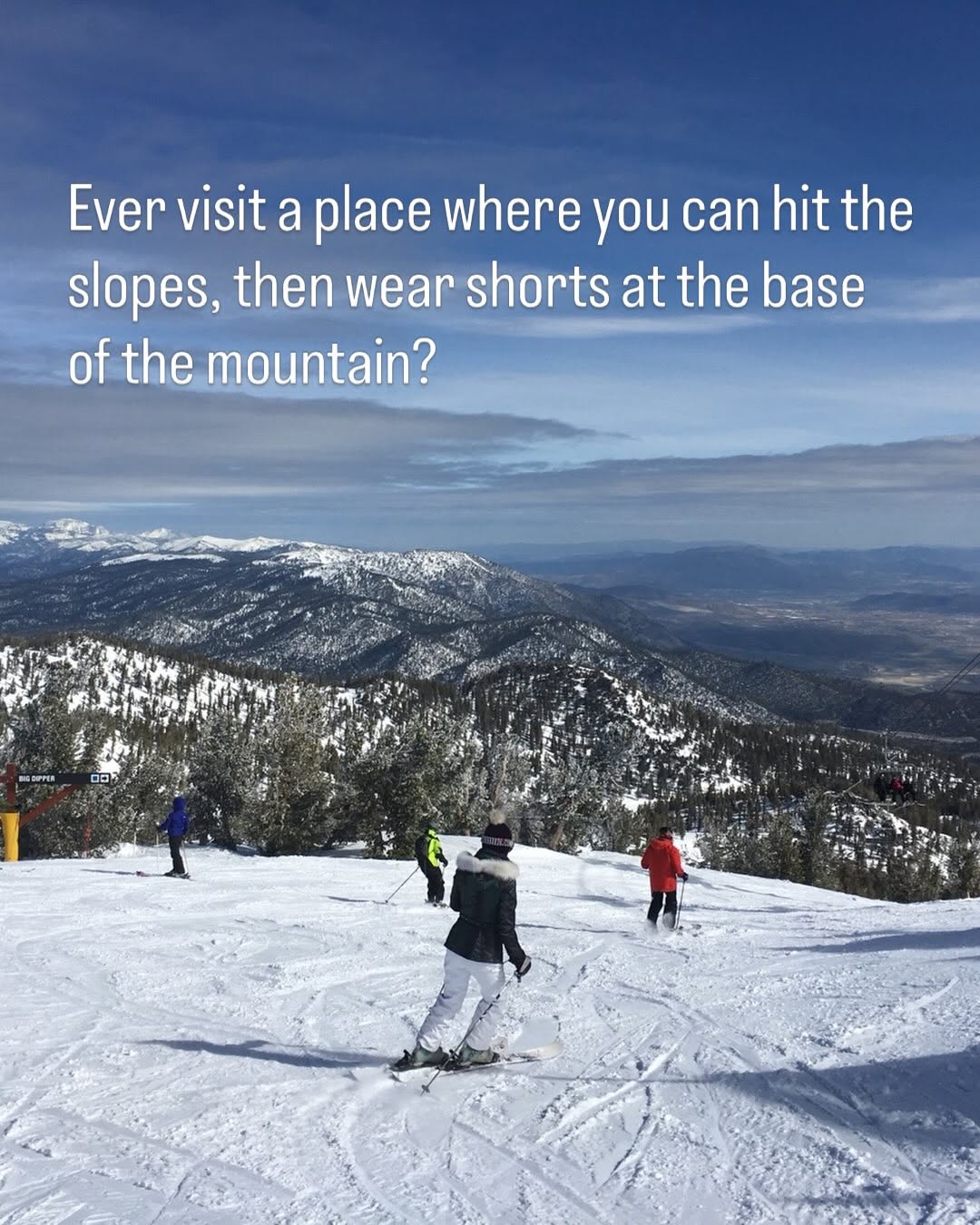 Skiers on a snowy mountain slope with a snow-free valley in the distance